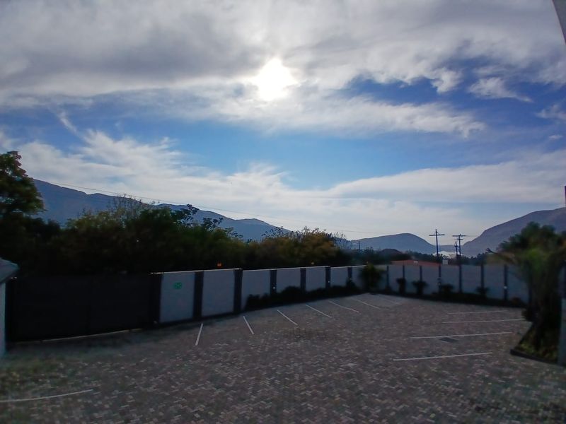 A paved parking area with marked bays, enclosed by a boundary wall, featuring scenic mountain views in the background.