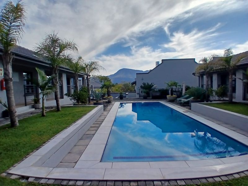 A well-maintained outdoor pool area featuring a rectangular swimming pool, paved surround, and landscaped garden beds with mountain views.