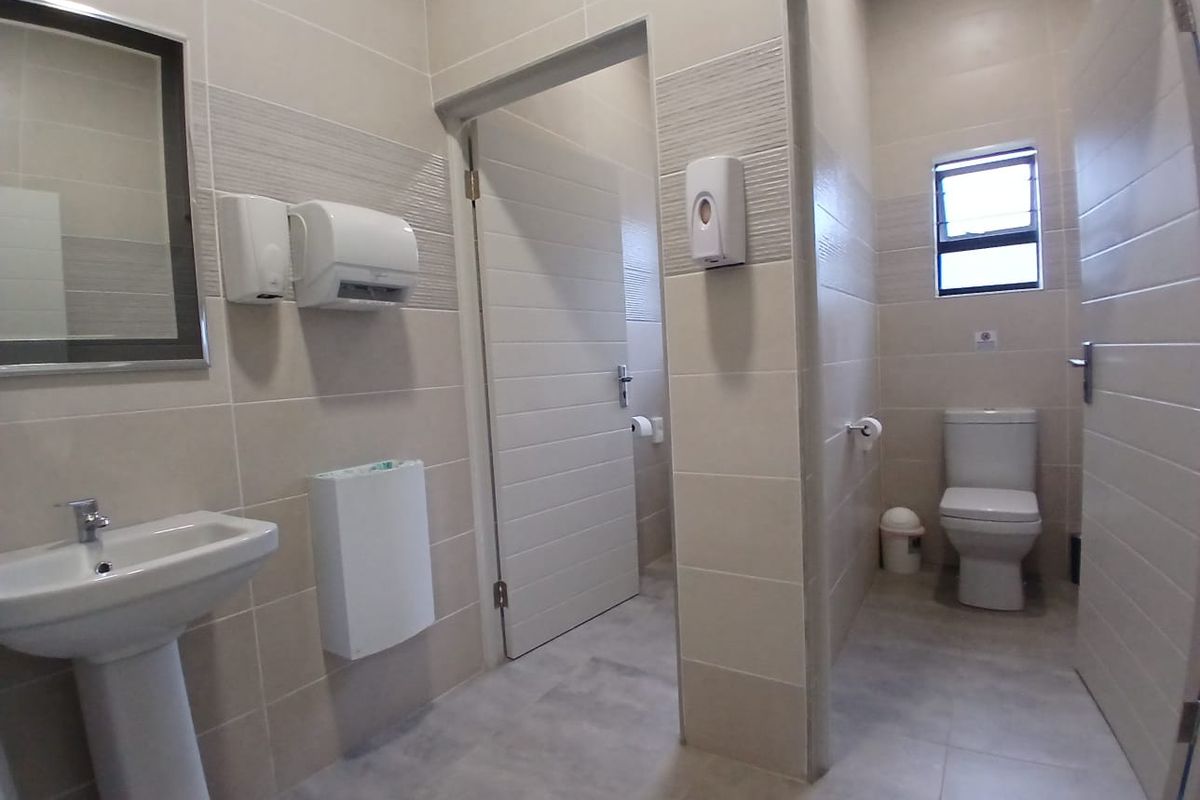 A clean, modern communal bathroom featuring tiled walls and floors, a pedestal basin, and a private toilet cubicle.