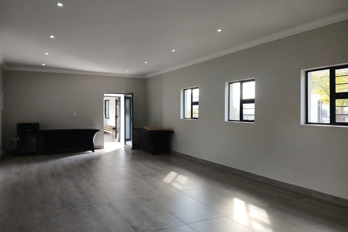 A spacious, empty living area featuring neutral tiled flooring, recessed downlighting, and large windows that provide ample natural light.