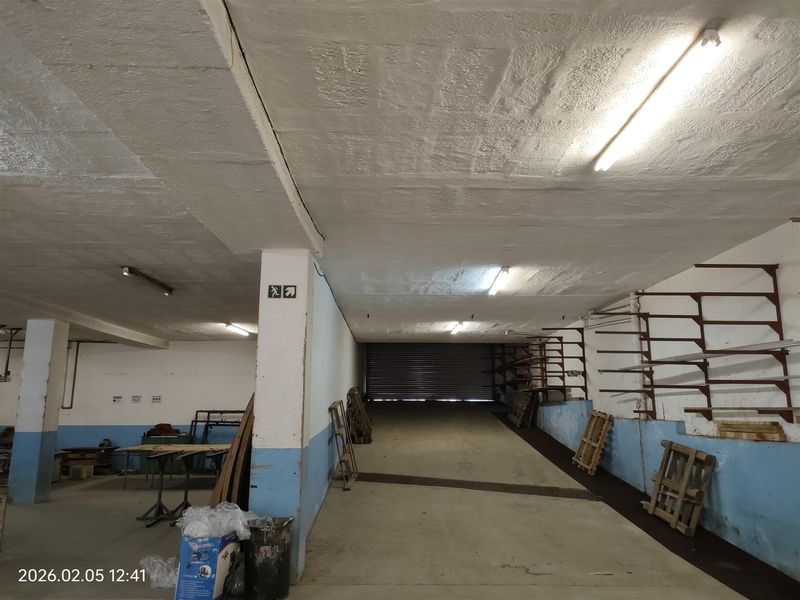 Spacious industrial garage or warehouse area featuring concrete flooring, roller shutter access, and wall-mounted shelving brackets, suitable for storage or workshop use.