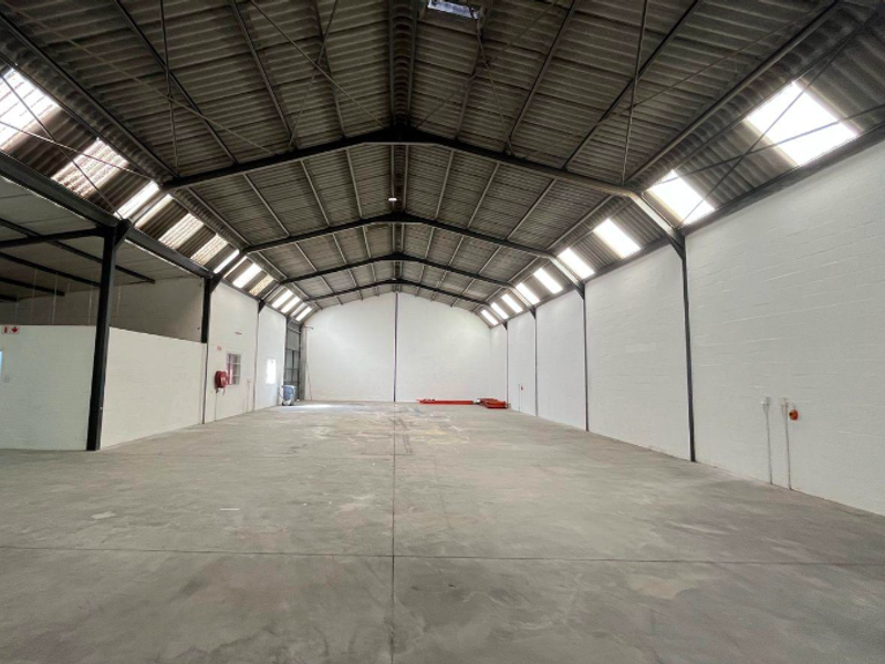 Spacious industrial warehouse unit featuring high ceilings with exposed steel trusses, abundant natural light from skylights, and durable concrete flooring.