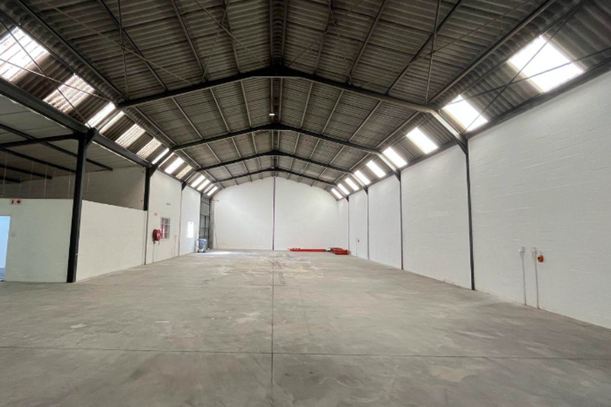Spacious industrial warehouse unit featuring high ceilings with exposed steel trusses, abundant natural light from skylights, and durable concrete flooring.