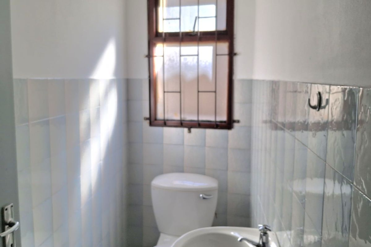 A compact bathroom featuring a white toilet, pedestal basin with chrome taps, and tiled walls with a small window.