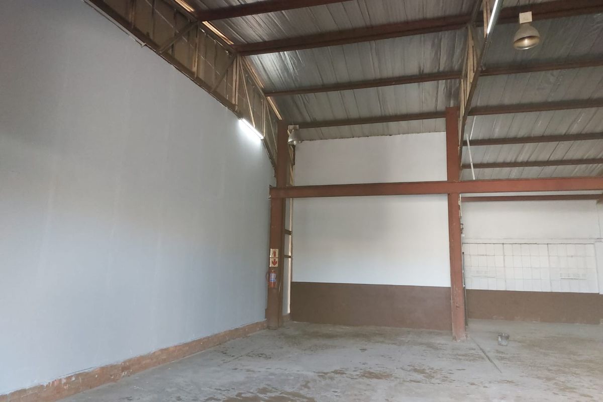 Spacious industrial warehouse unit featuring high exposed steel truss ceilings, concrete flooring, and functional wall-mounted fire safety equipment.