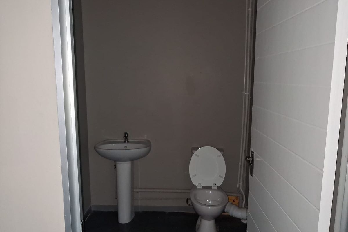 A functional office restroom featuring a pedestal sink and a standard toilet, with visible plumbing infrastructure.
