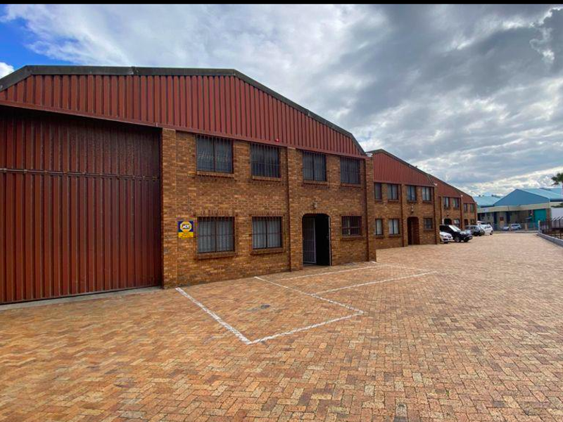 Industrial property featuring a face brick facade, large roller shutter door, security-barred windows, and a spacious paved driveway area.