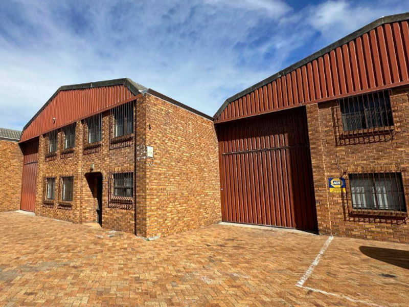 Industrial property exterior featuring face brick construction, corrugated metal roofing, security window bars, and a large roller shutter door with paved frontage.