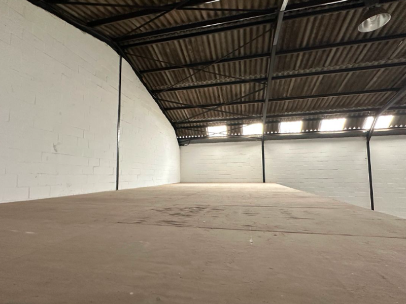 An elevated mezzanine storage or workspace area featuring exposed steel trusses, corrugated roofing, skylights, and painted masonry walls within an industrial setting.