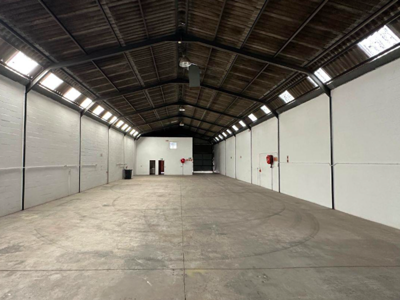 Spacious industrial warehouse unit featuring high ceilings with exposed steel trusses, natural light from skylights, and durable concrete flooring.