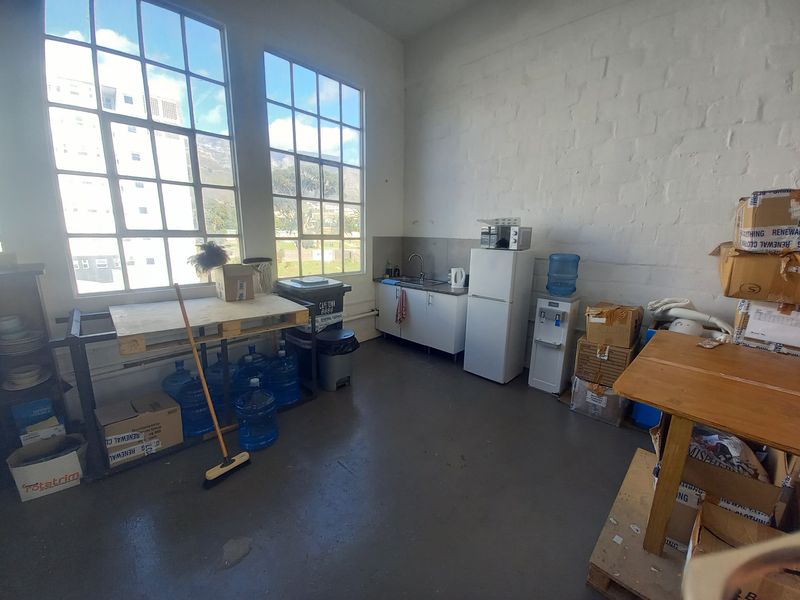 Industrial-style kitchenette featuring large steel-framed windows, painted brick walls, and basic cabinetry with a stainless steel sink.