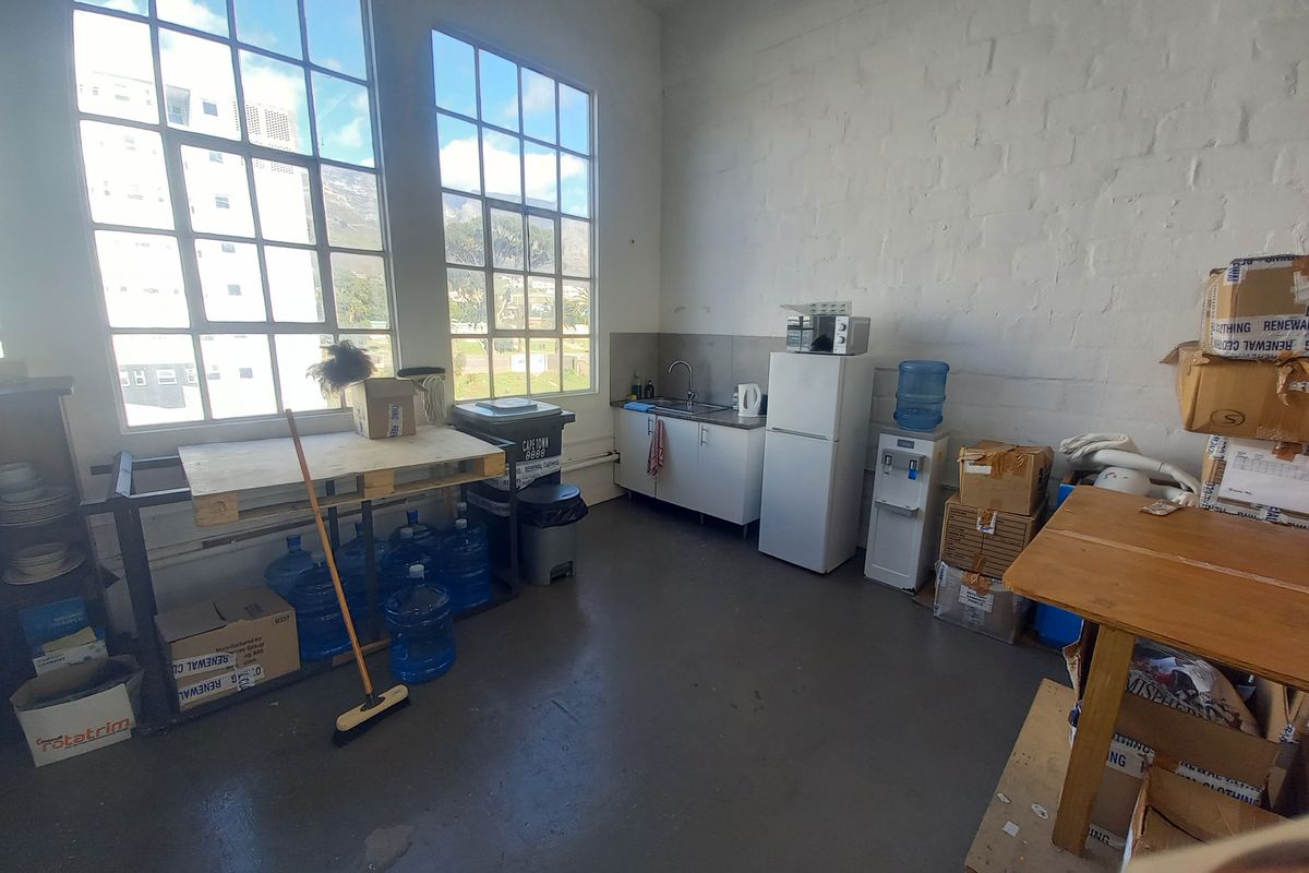 Industrial-style kitchenette featuring large steel-framed windows, painted brick walls, and basic cabinetry with a stainless steel sink.