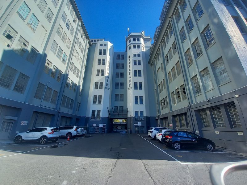 A wide-angle view of the Tollgate industrial building facade featuring multi-story architecture, industrial windows, and an asphalt parking courtyard.