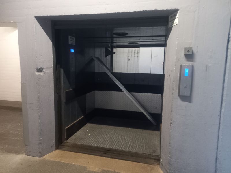 Industrial freight elevator with metal checker plate flooring and wall cladding, showing signs of heavy use and wear.