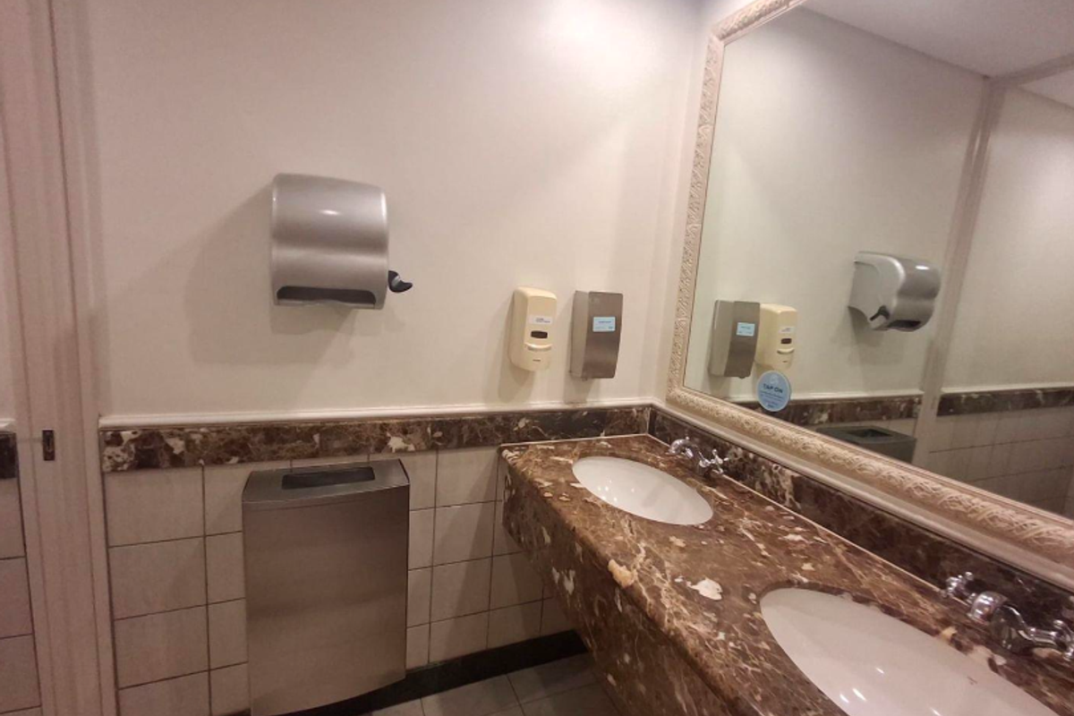 A commercial office restroom featuring a marble vanity countertop with dual integrated sinks, wall-mounted soap dispensers, and a paper towel dispenser.