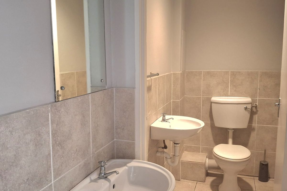 A functional office restroom featuring two wall-mounted ceramic basins, a standard toilet, and neutral tiled flooring and wall accents.