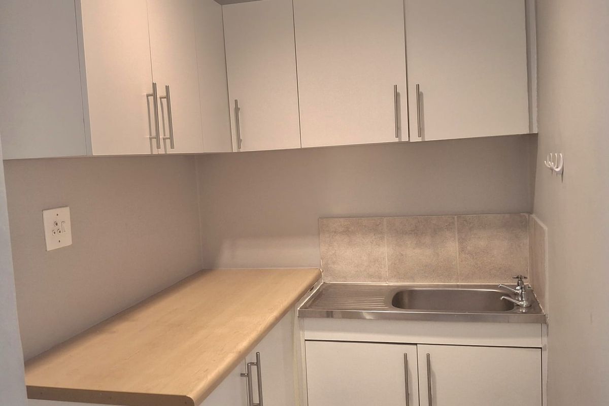A compact kitchenette area featuring white cabinetry, a light wood-look countertop, and a stainless steel sink with a tiled splashback.