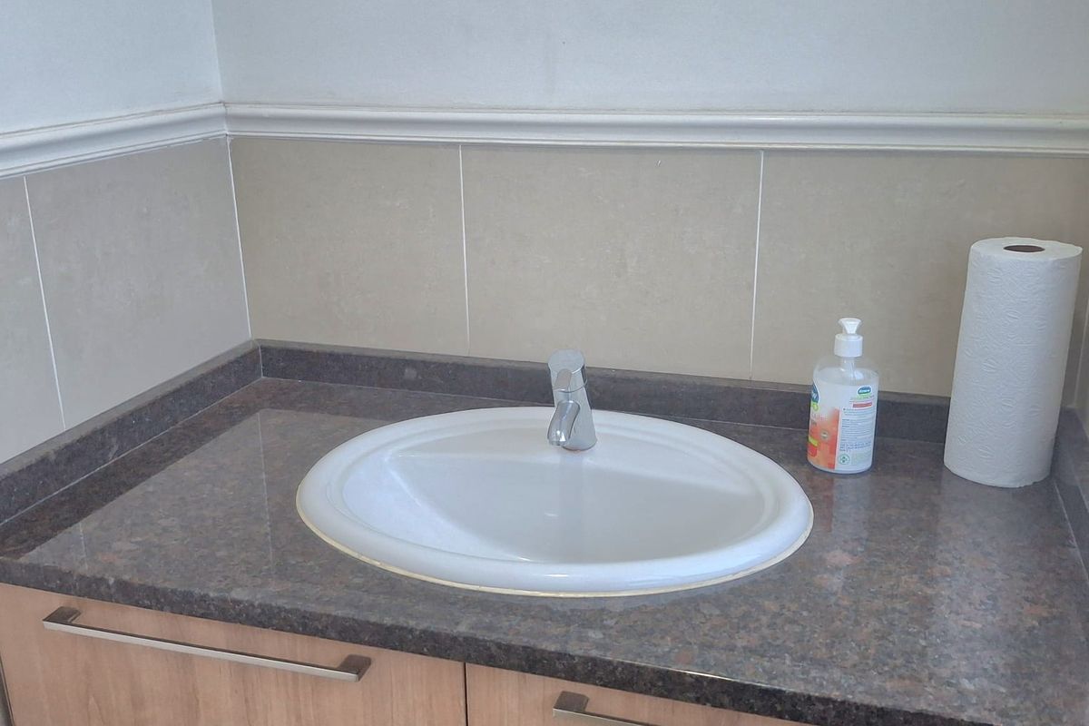 A functional office bathroom vanity featuring a drop-in sink, dark stone-look countertop, and wood-grain cabinetry with modern hardware.