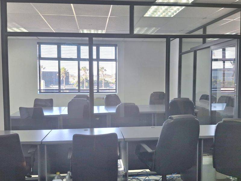 A partitioned office space featuring glass walls, suspended ceiling tiles, and integrated desk workstations, providing a functional professional environment.