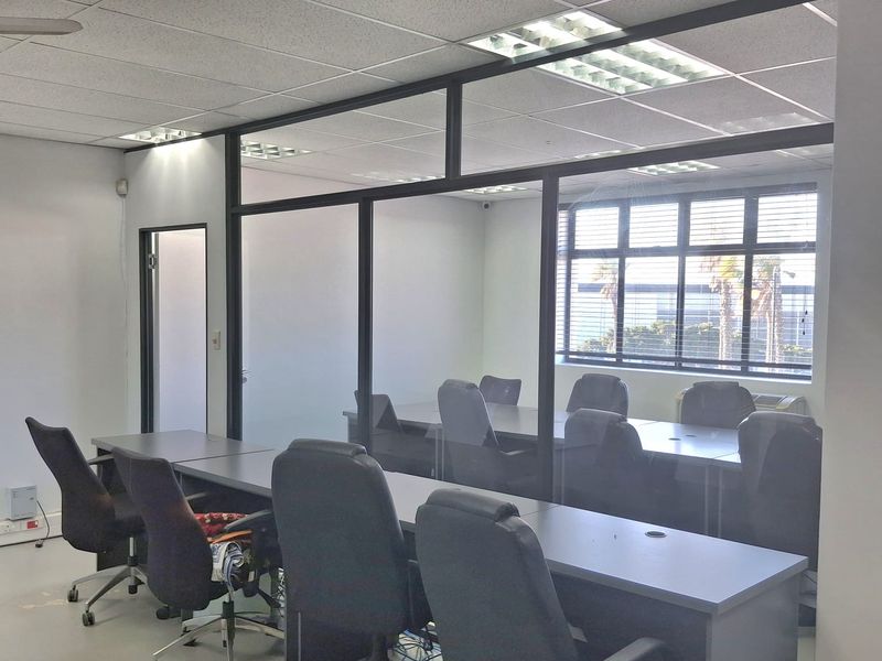 A professional office space featuring a glass-partitioned meeting room, suspended acoustic ceiling tiles, and integrated fluorescent lighting.