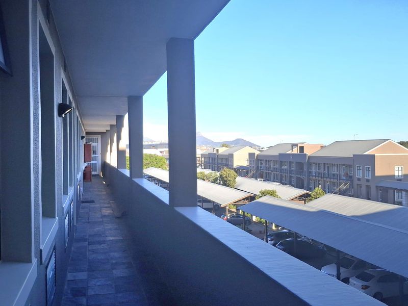A covered exterior walkway or balcony overlooking the office complex parking area with mountain views in the distance.
