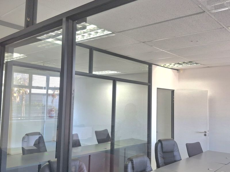 A modern office space featuring glass partition walls, suspended acoustic ceiling tiles, and integrated recessed lighting, creating a professional and bright work environment.
