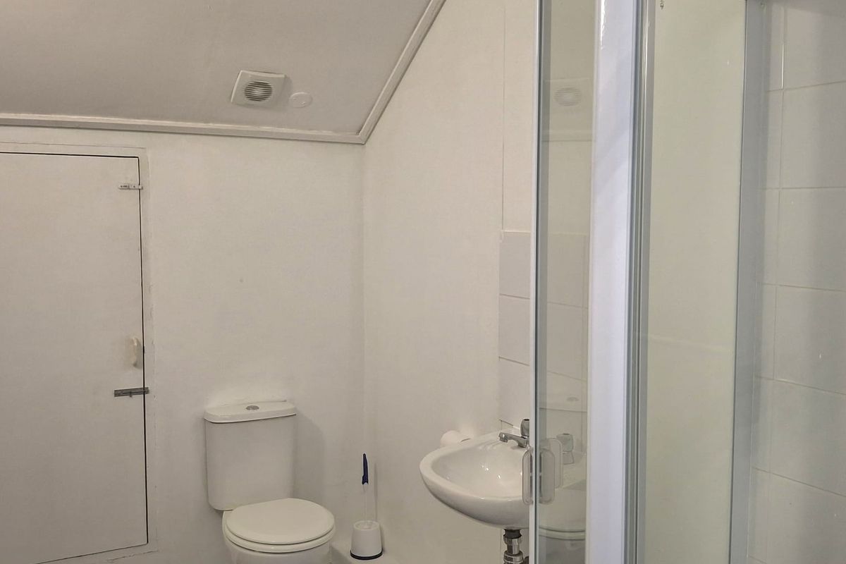 A compact bathroom featuring a shower enclosure, wall-mounted basin, and toilet, finished with tiled flooring and a sloped ceiling.