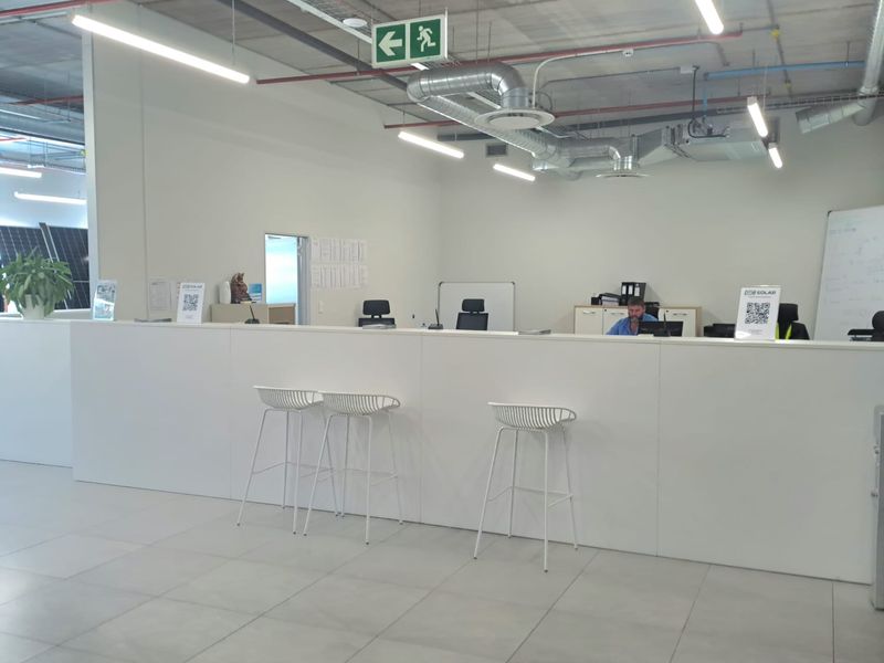 Modern industrial office space featuring an open-plan reception area with exposed concrete ceilings, industrial ducting, and tiled flooring.