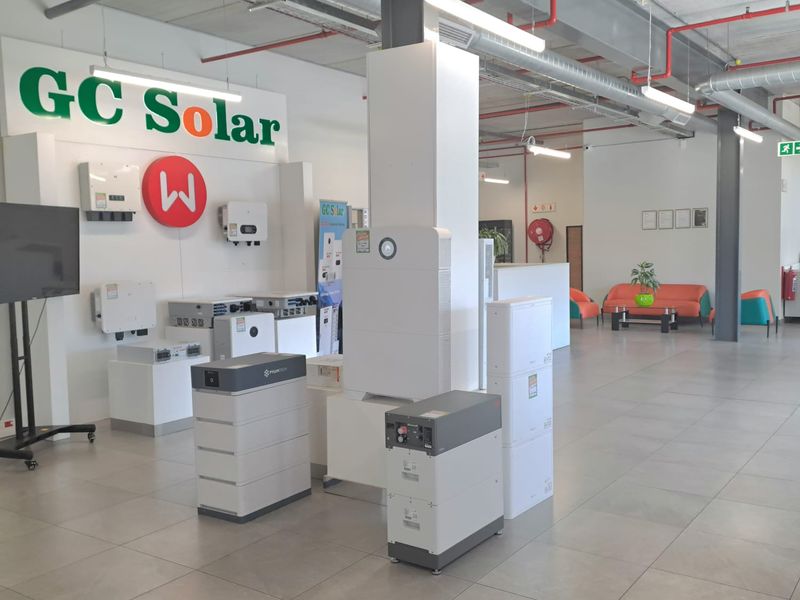 Spacious industrial showroom featuring exposed ceiling infrastructure, tiled flooring, and a dedicated display area for solar energy equipment and battery storage systems.