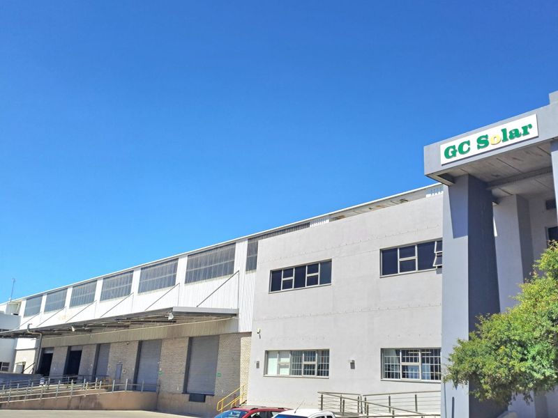 Exterior view of a modern industrial warehouse facility featuring loading bays, large roller shutter doors, and a dedicated office entrance area.