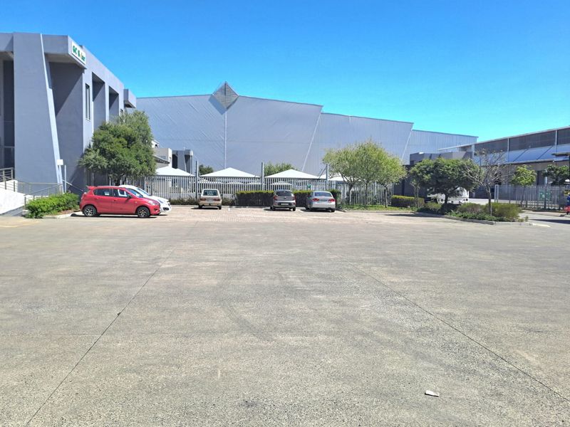 A wide-angle view of the industrial property exterior, featuring a large concrete parking area and modern grey facade building structures.