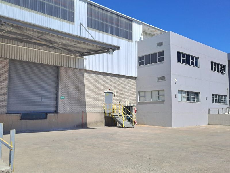Industrial warehouse exterior featuring a large roller shutter door, loading bay canopy, and adjacent multi-level office block with concrete yard space.