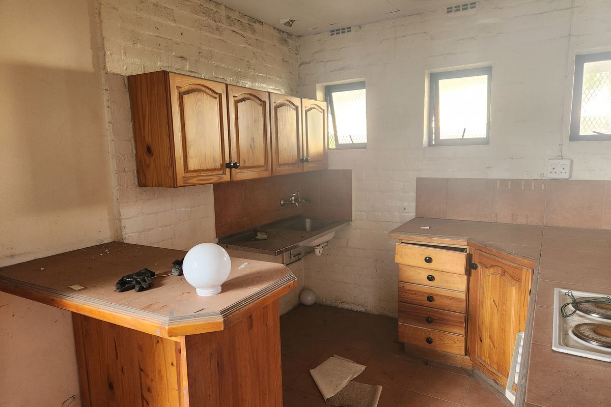 A dated kitchen area featuring wooden cabinetry, tiled countertops, and a stainless steel sink, requiring significant renovation and modernization.