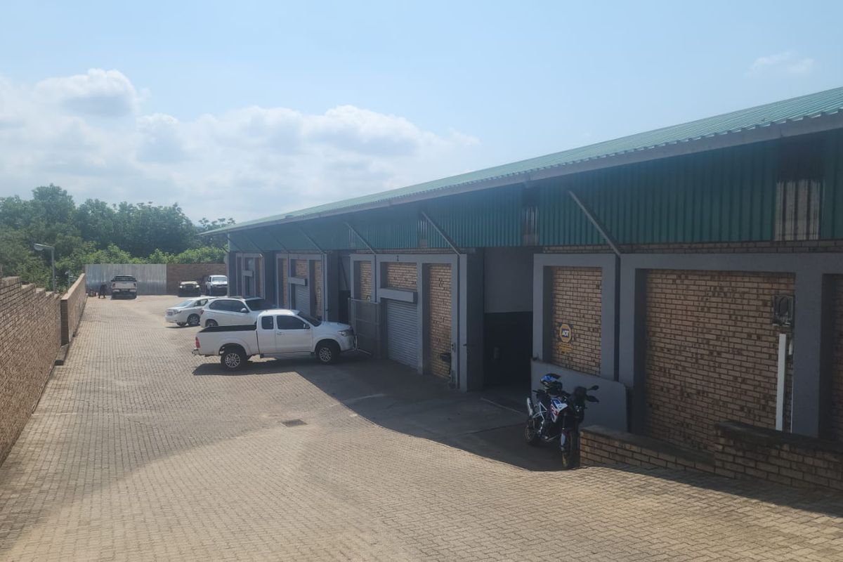 Exterior view of an industrial warehouse complex featuring brick facade, roller shutter doors, and a paved driveway area.