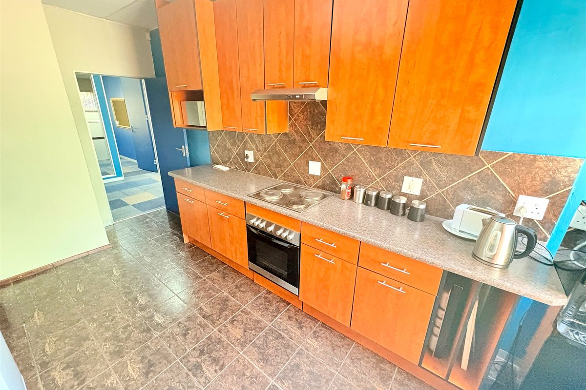 A functional office kitchenette featuring wood-veneer cabinetry, a built-in oven, electric hob, extractor fan, and tiled flooring.