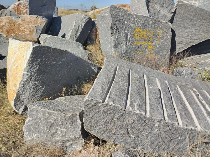 A pile of large, quarried stone blocks situated on the farm property, showing natural rock textures and some surface markings.