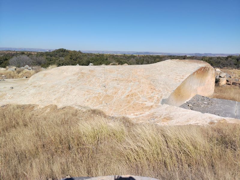 A wide-angle view of the natural farm landscape featuring a large exposed rock formation and surrounding dry grassland.