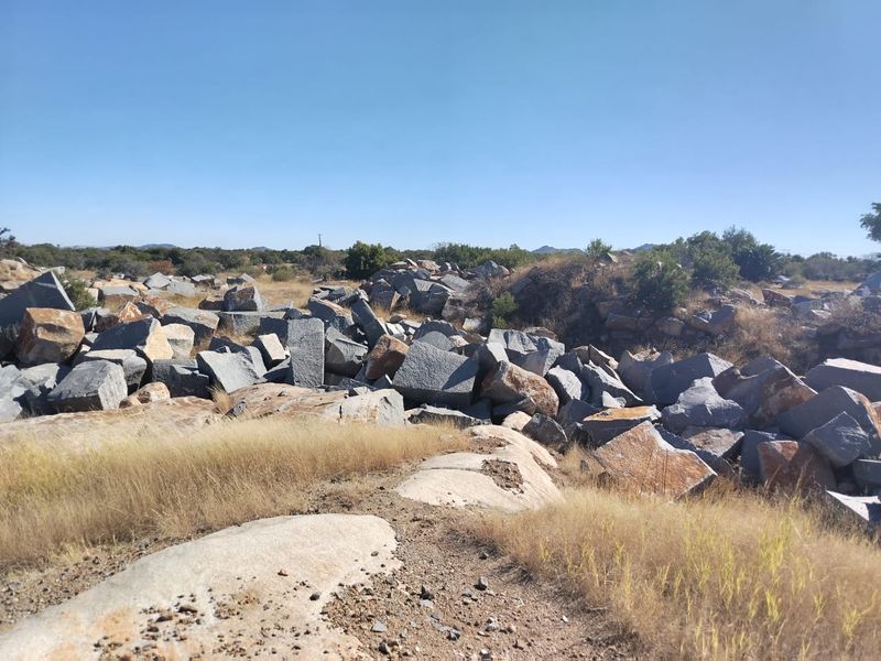 A view of the natural farm landscape featuring large rock formations and dry indigenous vegetation under a clear blue sky.