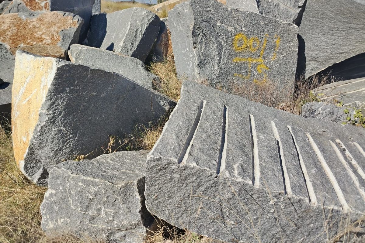 A pile of large, quarried stone blocks situated on the farm property, showing natural rock textures and some surface markings.