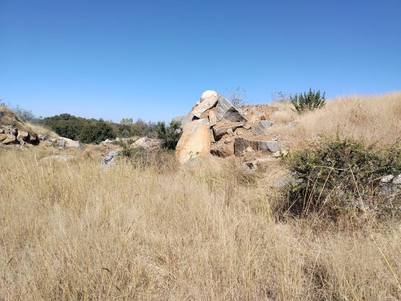 A view of the natural landscape on the farm property, featuring indigenous dry grass and prominent rock formations under a clear blue sky.