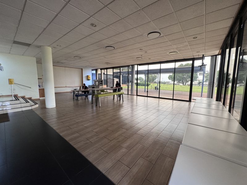 Spacious open-plan industrial office area featuring large floor-to-ceiling windows, modern tiled flooring, and a suspended ceiling with recessed lighting.