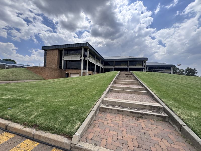 Exterior view of a multi-level industrial office building featuring a brick facade, metal roofing, and a central concrete staircase leading to the entrance.