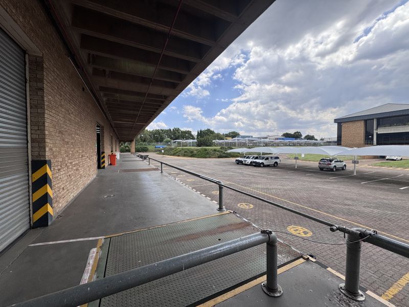 Industrial loading bay area featuring a roller shutter door, concrete canopy, and access to a paved parking lot with shade cloth carports.