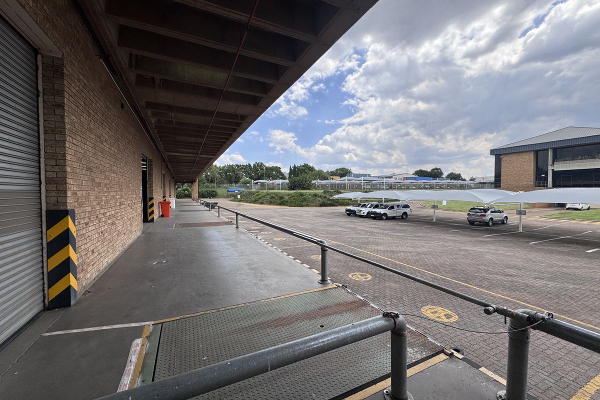 Industrial loading bay area featuring a roller shutter door, concrete canopy, and access to a paved parking lot with shade cloth carports.