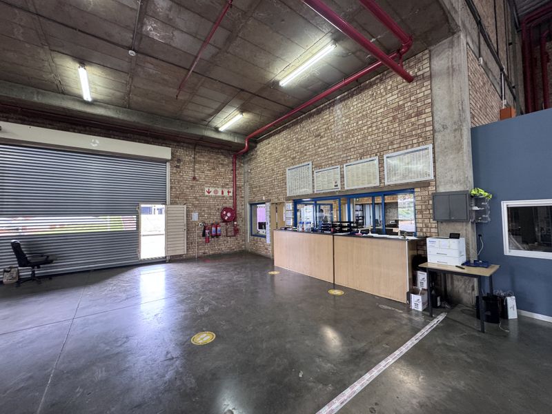 Industrial utility space featuring a large roller shutter door, exposed concrete ceilings, face brick walls, and a built-in reception counter.