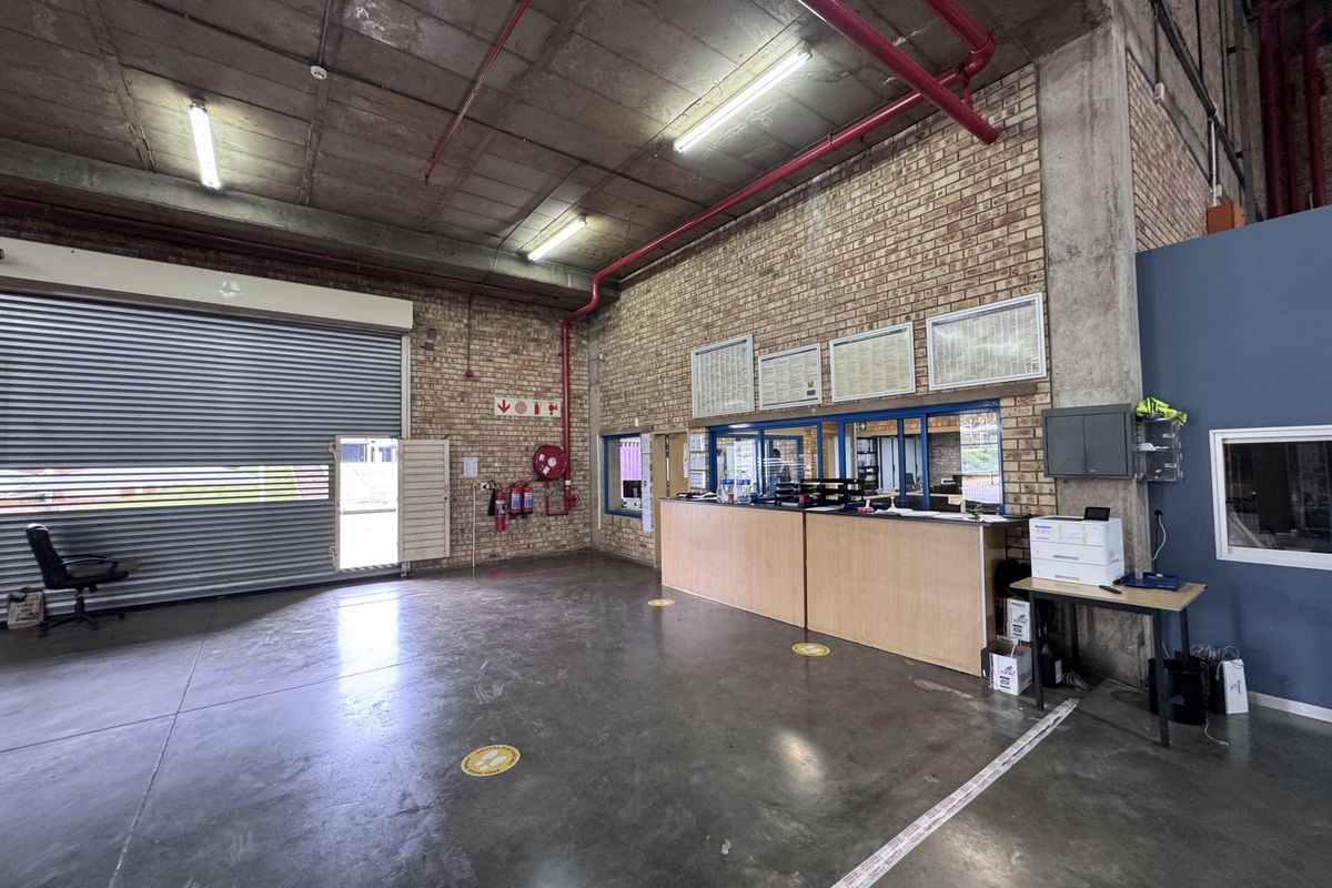 Industrial utility space featuring a large roller shutter door, exposed concrete ceilings, face brick walls, and a built-in reception counter.
