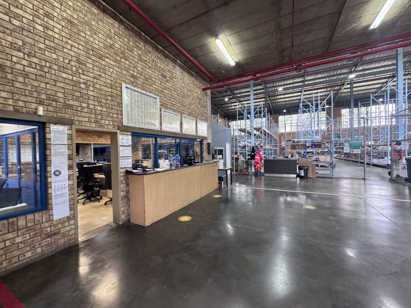 Industrial warehouse space featuring exposed brick walls, concrete flooring, high ceilings with fire suppression systems, and integrated office reception area with industrial racking.