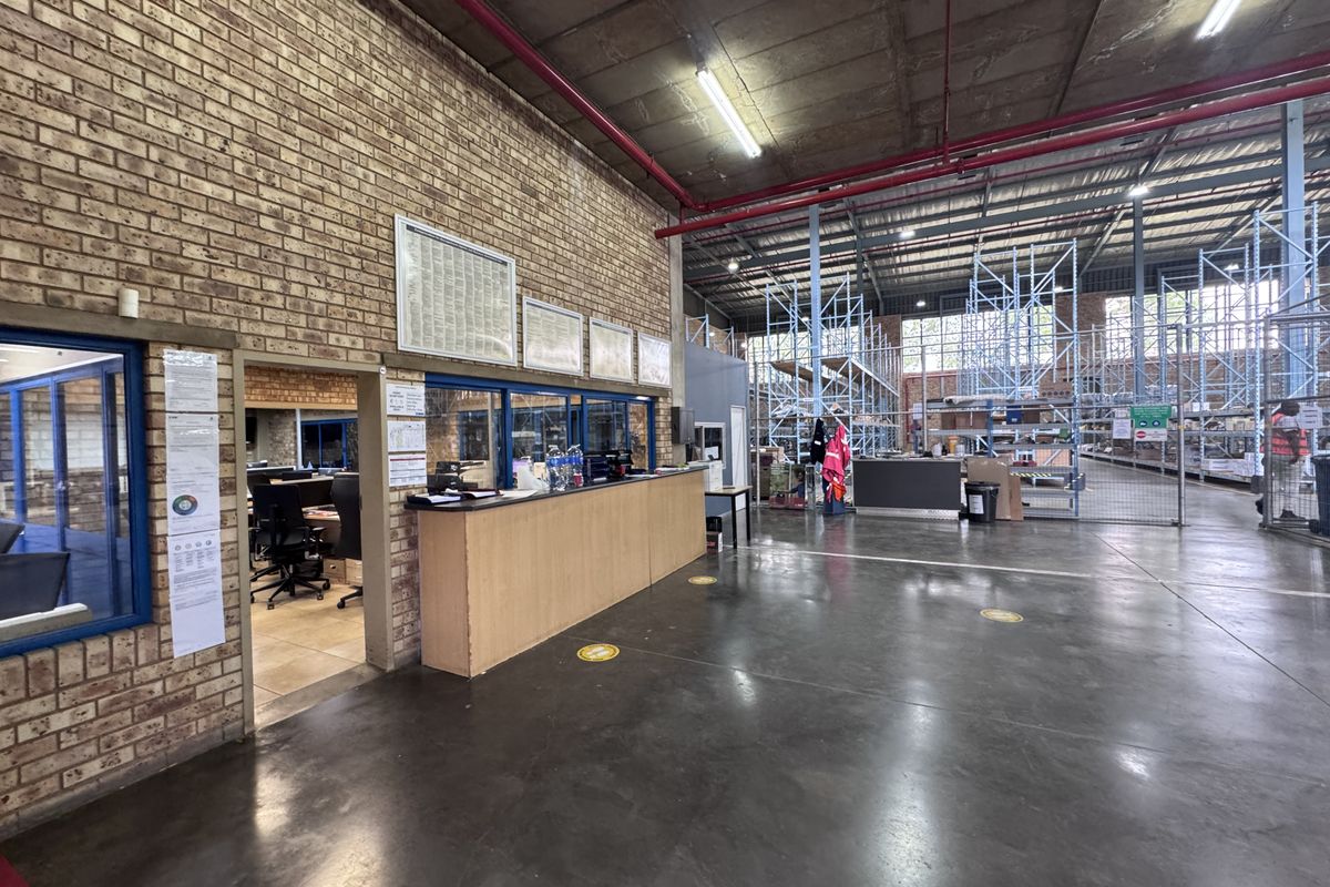 Industrial warehouse space featuring exposed brick walls, concrete flooring, high ceilings with fire suppression systems, and integrated office reception area with industrial racking.