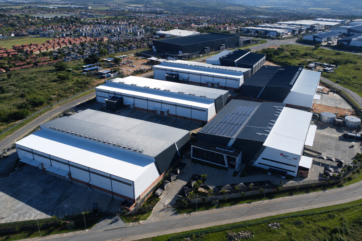 Aerial view of a large industrial warehouse complex featuring multiple buildings, expansive paved yard areas, and solar panel installations on the roof.