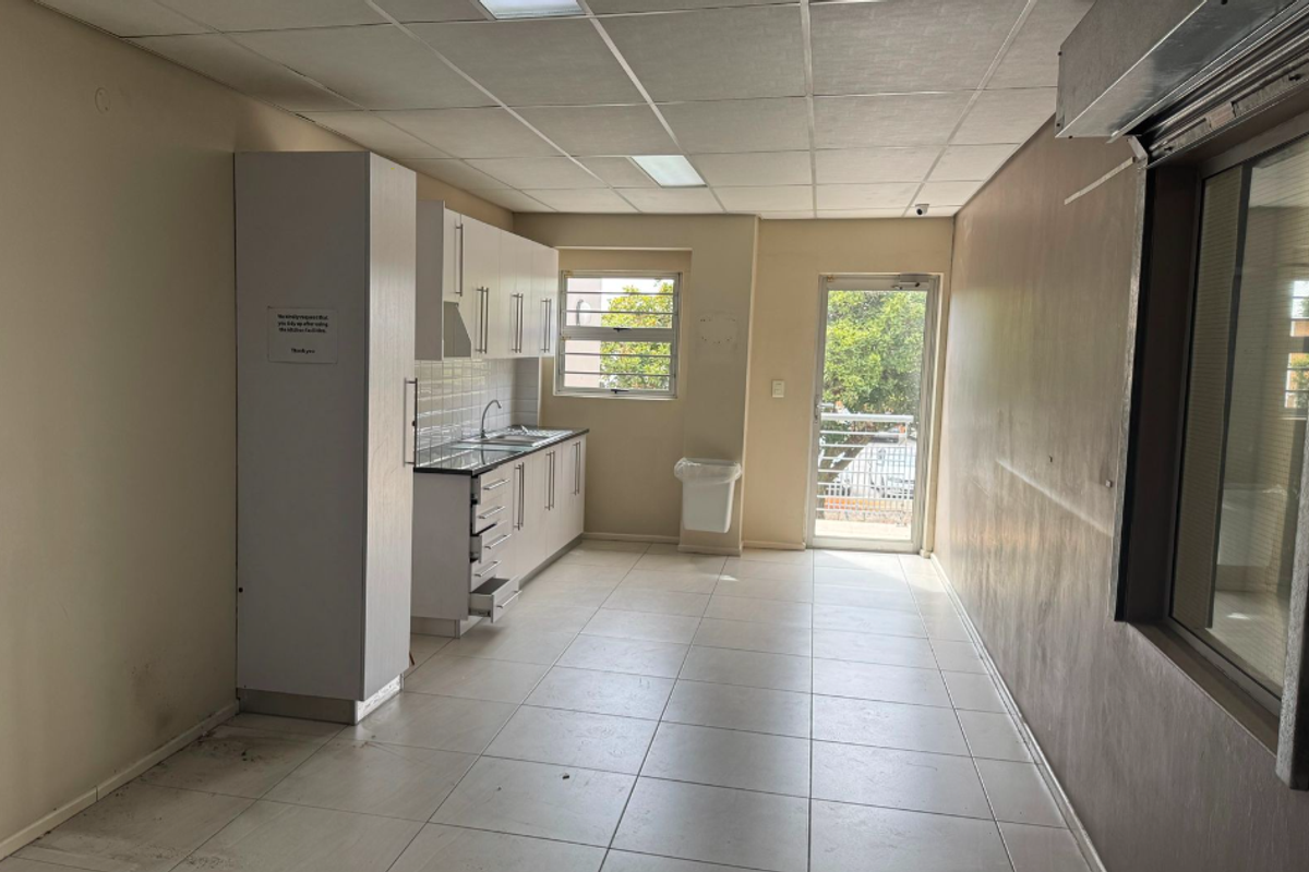 A functional industrial kitchenette featuring white cabinetry, tiled flooring, a drop ceiling, and direct access to an exterior balcony area.